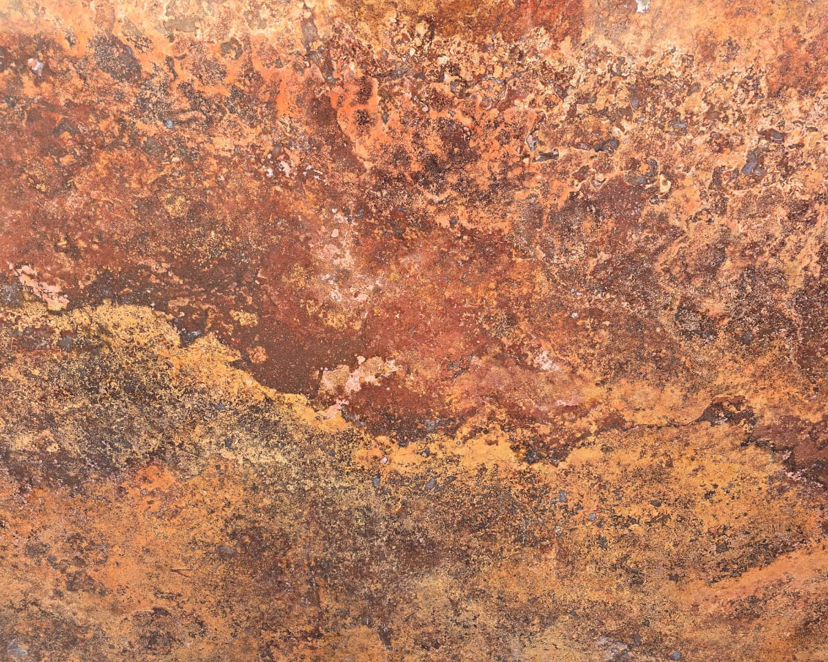 A close-up of a textured surface with a mottled pattern of rust orange, brown, and golden yellow tones.